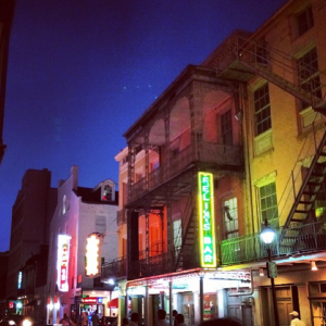 Along the street where the Acme Oyster House is located, you'll find brightly lit bars and tourists lining up for drinks (Photo by Nicky Diaz).